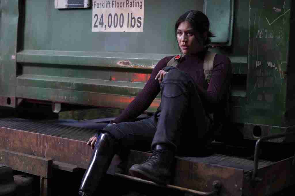 Maya Lopez "Echo" sat with one knee up in front a shipping container.
