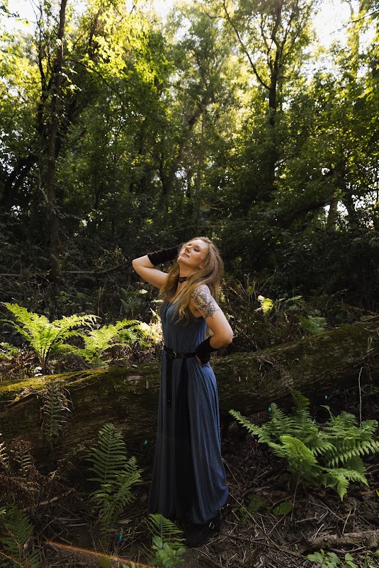 Courtney in a long flowing blue dress and elbow length black gloves in a forest