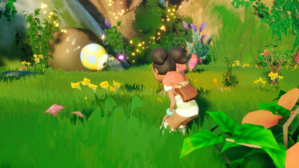 Ikonei Island: A young, dark skinned woman, with her hair in two "space buns", standing in bright green grass, bent over talking to a small, round, polka dot bee like creature. The bee has a little glowing trail around it as it has just done a flip in the air in the shape of a heart.