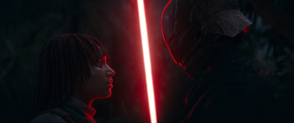 one of the twins stands face to face with a masked sith, red lightsaber ignited between them- The Acolyte