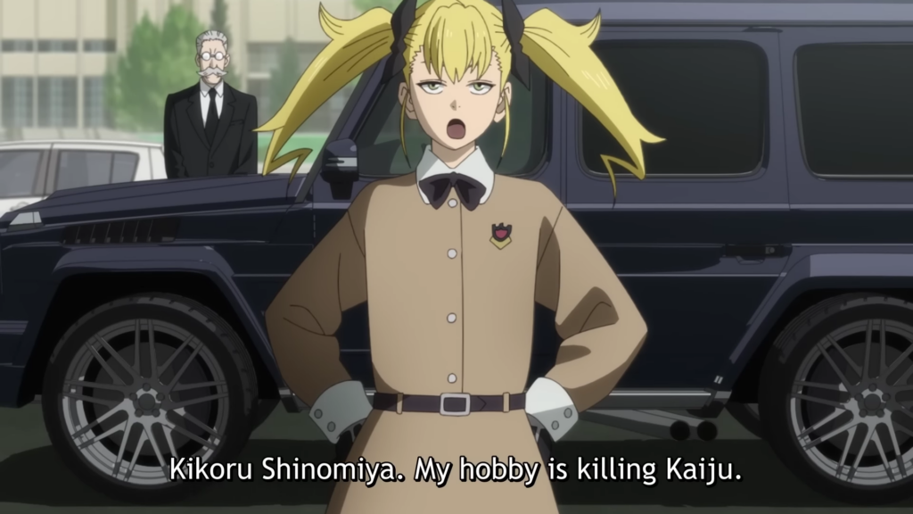 a small blonde young lady stands beside and expensive car and butler. Subtitle text reads "Kikoru Shinomiya. My Hobby is killing Kaiju"  Kaiju No. 8