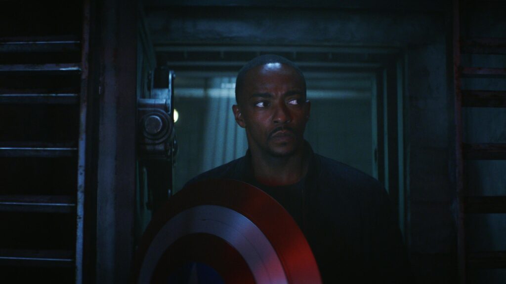 Sam steps through a dark doorway, shield held at the ready.  Captain America Brave New World 