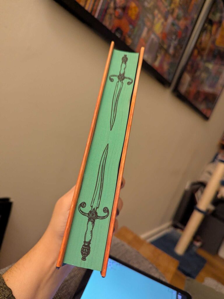 A photograph of the sprayed edges of Brigands & Breadknives. It's green with two embossed black swords.