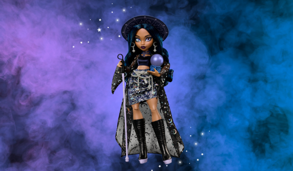 Monster High - a dark skinned witch who has a walking cane in one hand and a crystal ball in the other. She has dark hair with moons and stars covering a cape she is wearing. 